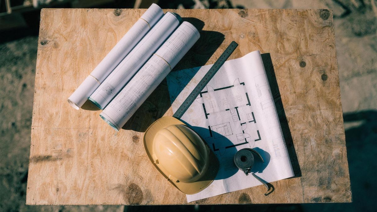 Construction drawings and site tools on a plywood table at an All Pro Alliance site